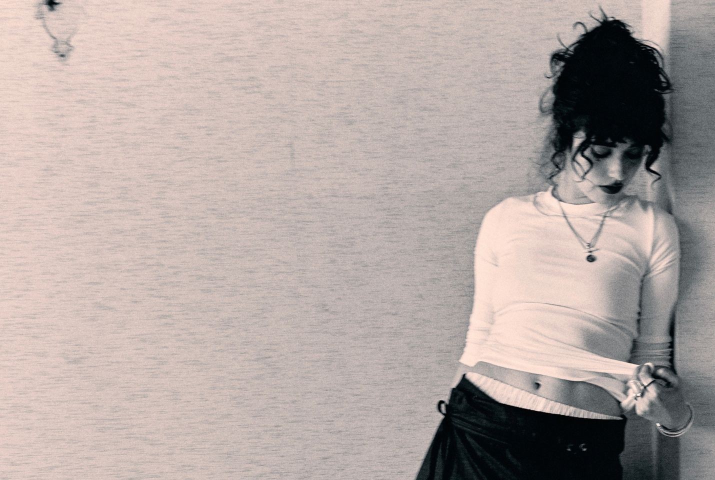 A woman with dark curly hair leaning against a wall